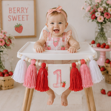 Load image into Gallery viewer, A baby girl sitting in a high chair decorated for a berry first birthday, wearing a strawberry-patterned dress and a pink bow headband. The high chair has a decorative front banner with a pink number 1, red and white tassels, and a red-and-white berry garland.
